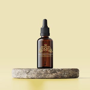 May include: A brown glass bottle with a black dropper top and a gold label that reads "MAGESTIC SO BEAUTY PRODUCTS GROW, THRIVE, & GLOW". The bottle is sitting on a gray stone surface.