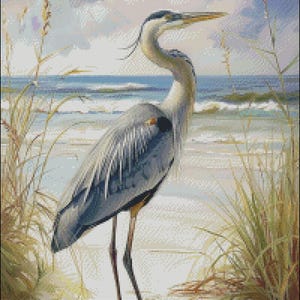 May include: A blue heron stands on a sandy beach with tall grasses in the foreground and a blue sea in the background.