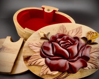 May include: A wooden puzzle box with a carved rose design. The box is made of light wood and has a red velvet interior. The lid of the box is open, revealing the interior.