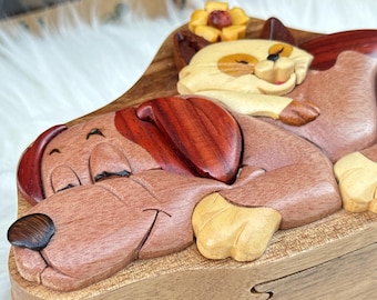 May include: A wooden puzzle featuring a sleeping dog and cat. The dog is brown with dark red ears, and the cat is cream-colored with a yellow flower. The puzzle is made of various wood tones and has a detailed, carved design.