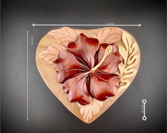 May include: A wooden heart-shaped puzzle box with a carved hibiscus flower design. The box is 12 cm wide and 5.7 cm tall.