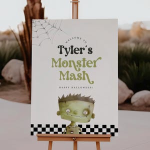May include: A wooden easel displays a sign with the text "Tyler's Monster Mash" in green and black lettering, with a cartoon Frankenstein's monster illustration. The sign includes a spiderweb graphic and the words "Happy Halloween!"
