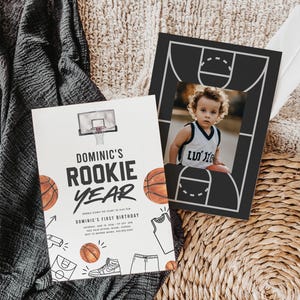 May include: A white invitation with a basketball theme for a first birthday party. The invitation features a basketball hoop, basketballs, and the text "Dominic's Rookie Year".