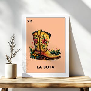 Puede incluir: Una carta de Loteria de estilo vintage con el número 22 y la palabra "LA BOTA" impresa en un fondo melocotón. La carta presenta una ilustración colorida de una bota vaquera amarilla con bordados florales rojos y amarillos.