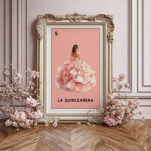 Op de afbeelding: Een ingelijste print met een jonge vrouw in een roze quinceañera-jurk. Het kunstwerk heeft een roze achtergrond met het nummer "5" bovenaan en de woorden "LA QUINCEAÑERA" onderaan. De lijst is versierd met gouden details.