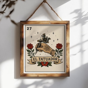 May include: A framed wall art print featuring a beige background with the number 27 in the top left corner. The illustration depicts a hand holding a tattoo machine, surrounded by red roses and green leaves, with the text EL TATUADOR on a banner.