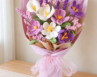 May include: A crochet flower bouquet featuring white calla lilies, purple crocuses, and small pink blossoms with green leaves. The arrangement is wrapped in light pink and brown paper, tied with a sheer pink ribbon, and presented in a light pink vase.
