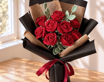 Puede incluir: Un ramo de rosas rojas de ganchillo con hojas de ganchillo de color verde claro. Las flores están envueltas en capas de papel de nido de abeja negro y marrón, aseguradas en la base con una cinta de satén rojo oscuro atada en un lazo central.
