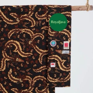 Può includere: Un tessuto nero con un motivo ripetuto di motivi floreali e fogliari marroni e beige. Il tessuto è drappeggiato su un'asta di legno. È visibile un cerchio verde con la scritta "RoyalJava". Diverse piccole etichette sono attaccate al tessuto.
