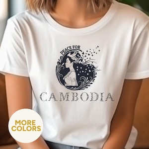 May include: White t-shirt with a circular graphic featuring a woman's profile, butterflies, and the text "PEACE FOR CAMBODIA." The shirt also has a "MORE COLORS" button.