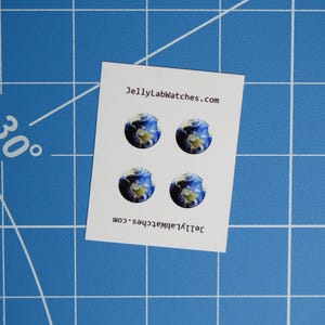 Puede incluir: Cuatro pegatinas redondas con una imagen de un globo terráqueo azul y verde. Las pegatinas están en una hoja de papel blanca con el texto "JellyLabWatches.com" impreso en la parte superior e inferior.