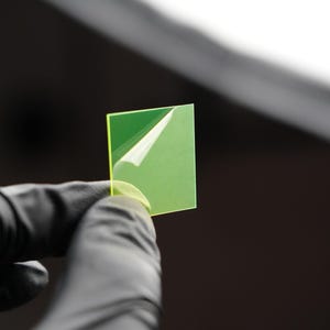 Puede incluir: Un trozo cuadrado de vidrio verde con una película protectora que se está despegando.