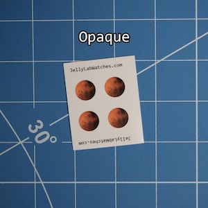 May include: A white sticker sheet with four circular stickers depicting the planet Mars. The stickers are orange and brown. The text "Opaque" is above the sticker sheet. The website "JellyLabWatches.com" is printed on the sticker sheet.