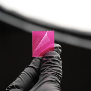 Op de afbeelding: Een vierkant roze plakvel met een hoek die is teruggevouwen om de kleverige kant te laten zien.