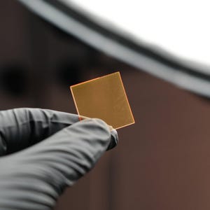 May include: A small, square, translucent, orange-colored glass or plastic sheet.