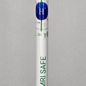 May include: A white pen with a green "MRI SAFE" label and a diagram of a hydrogen atom with an arrow pointing up. The pen has an orange top and a black base.