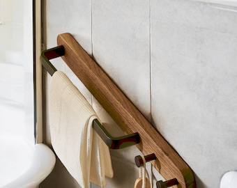 May include: A wooden towel rack with a black metal towel bar and two hooks. A white towel is hanging on the bar and a wooden brush is hanging on one of the hooks.
