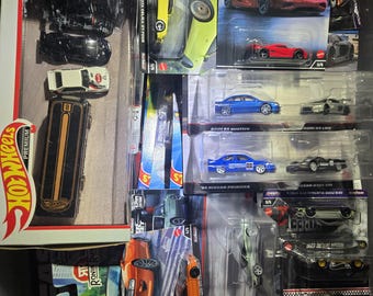 May include: A collection of various Hot Wheels die-cast toy cars in their original blister packaging and a boxed set. The assortment includes multiple sports cars, sedans, and racing vehicles in diverse colors like red, blue, orange, and black.