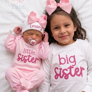 May include: A baby wearing a pink long-sleeve onesie with the text little sister and a white hat with the name Emory and a pink bow, next to a child wearing a white long-sleeve shirt with the text big sister and a pink hair bow.