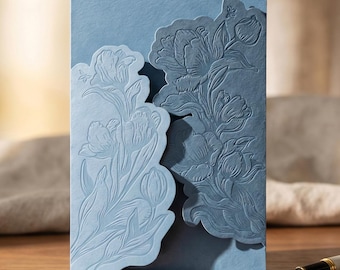 May include: A light blue invitation card with a floral design. The card features an embossed tulip pattern on the front, with a die-cut edge. The card is made of textured paper and is suitable for weddings or special events.