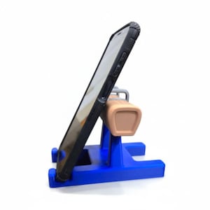 Könnte beinhalten: Ein blau-beiger Telefonständer mit einem Telefon in einer schwarzen Hülle. Der Ständer hat einen blauen Sockel und eine beige Telefonauflage. Das Telefon ist zum Betrachten abgewinkelt.