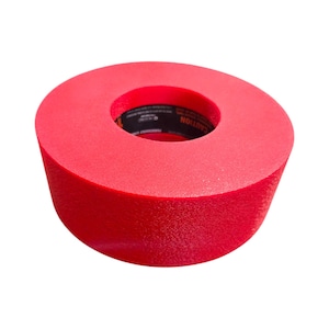 May include: A bright red, cylindrical abrasive wheel with a central hole. The wheel has a textured surface and a black label with white text that reads "CAUTION". This tool is likely used for grinding or polishing.