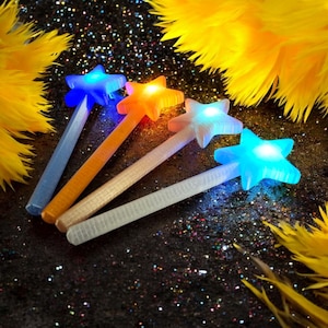 May include: Four star-shaped wands with glowing LED lights in blue, orange, and white. The wands have textured handles and are set against a dark, glittery background with yellow feather accents. These are ideal for parties or costumes.