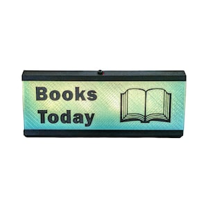May include: A rectangular sign with the words "Books Today" in black, above a black outline of an open book. The background is a gradient of green and blue, with a black border.