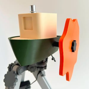 May include: A small, green and white toy boat with an orange propeller. The boat is mounted on a tripod stand.