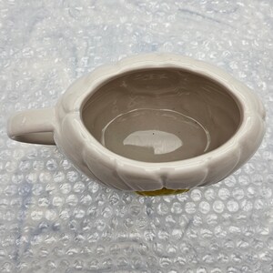 Peut inclure: Une tasse en c&eacute;ramique blanche avec une anse, en forme de fleur. L'int&eacute;rieur est de couleur gris clair et le fond a un accent jaune. La tasse est con&ccedil;ue avec un ext&eacute;rieur en forme de p&eacute;tale.