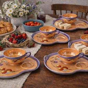 May include: A collection of vintage tea cups and saucers with a decorative design. The cups and saucers are orange with a purple trim. The table is set with pastries, fruit, and flowers, creating a charming and inviting atmosphere.
