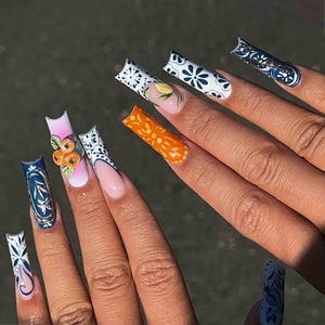May include: Long square-shaped artificial nails featuring a variety of designs including blue and white floral patterns, a solid orange nail with an embossed orange pattern, and a pink-to-white gradient nail adorned with three-dimensional orange fruit.