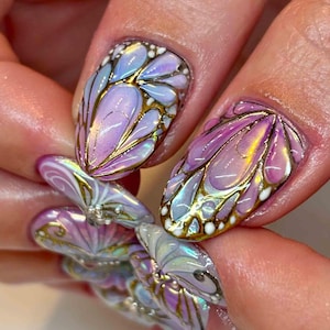 May include: Close-up of a hand with intricately designed nail art. The nails feature a butterfly wing design with iridescent purple, blue, and gold accents. The design is detailed with gold outlines and white dots, creating a 3D effect.