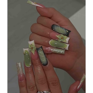 May include: A hand displaying long, square-shaped acrylic nails. The nails feature a variety of designs, including ombre effects, floral embellishments, and gold accents. Colors include pink, green, white, and a gradient of colors.