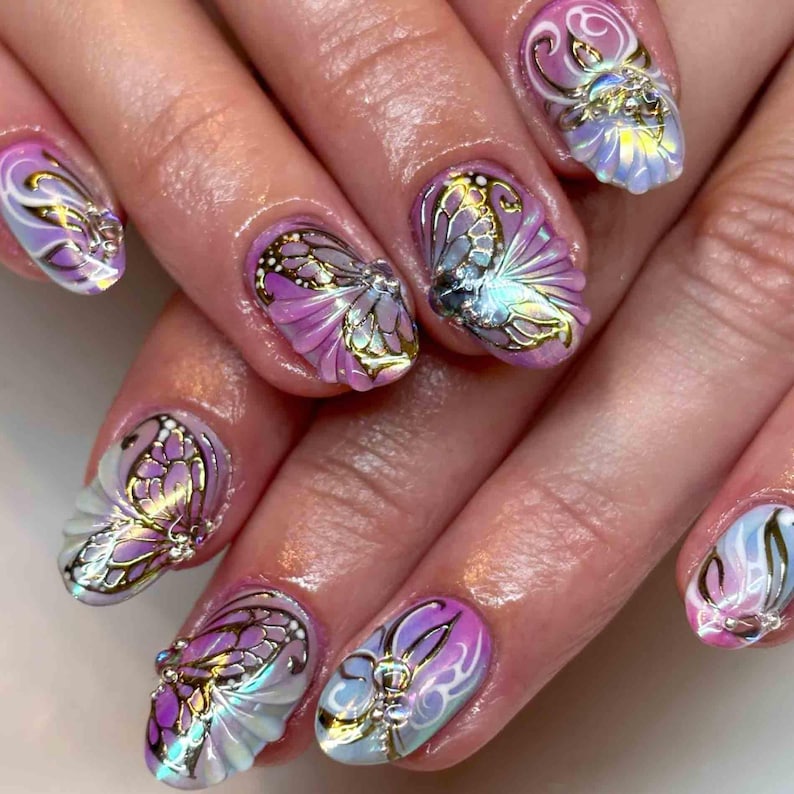May include: Close-up of a manicure featuring butterfly nail art. The nails are painted with a gradient of pink and white, and adorned with gold and silver butterfly designs. The butterfly wings have a shimmering, iridescent effect.