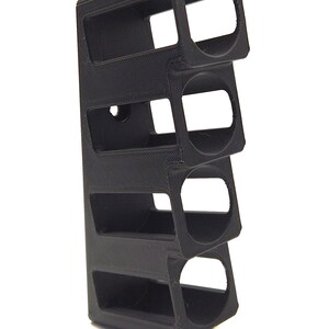 May include: A black, rectangular, 3D-printed object with four open compartments. The object has a textured surface and is designed to hold cylindrical items. The design is modern and minimalist.