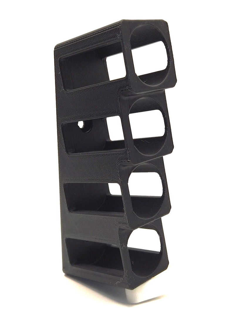 May include: A black, rectangular, 3D-printed object with four open compartments. The object has a textured surface and is designed to hold cylindrical items. The design is modern and minimalist.