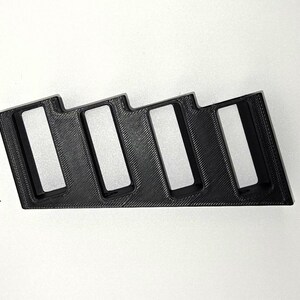 May include: A black, 3D-printed organiser with four rectangular slots. The organiser has a stepped design and is likely for holding small items. The material appears to be plastic, and the object is set against a white background.