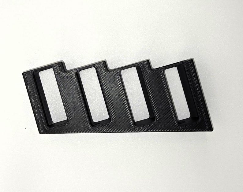 May include: A black, 3D-printed organiser with four rectangular slots. The organiser has a stepped design and is likely for holding small items. The material appears to be plastic, and the object is set against a white background.