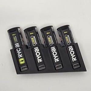 May include: A black 3D-printed battery holder with four Ryobi USB Lithium batteries. Each battery is black with white and yellow text, including "2Ah" and "USB Lithium". The holder has a slot for each battery.