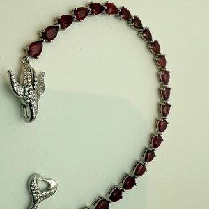 May include: A silver bracelet with a heart-shaped clasp and a row of pear-shaped red gemstones.