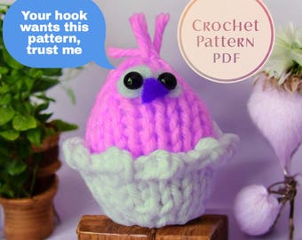 May include: A handmade, pink crochet bird with a purple beak and black eyes, sitting in a white, ruffled crochet cup. Text reads, "Your hook wants this pattern, trust me" and "Crochet Pattern PDF."