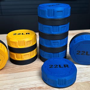 May include: A collection of cylindrical storage containers for 22LR ammunition, featuring yellow and blue plastic bodies with black textured grip bands. Each lid is embossed with the text 22LR in black, showing various stacking configurations.