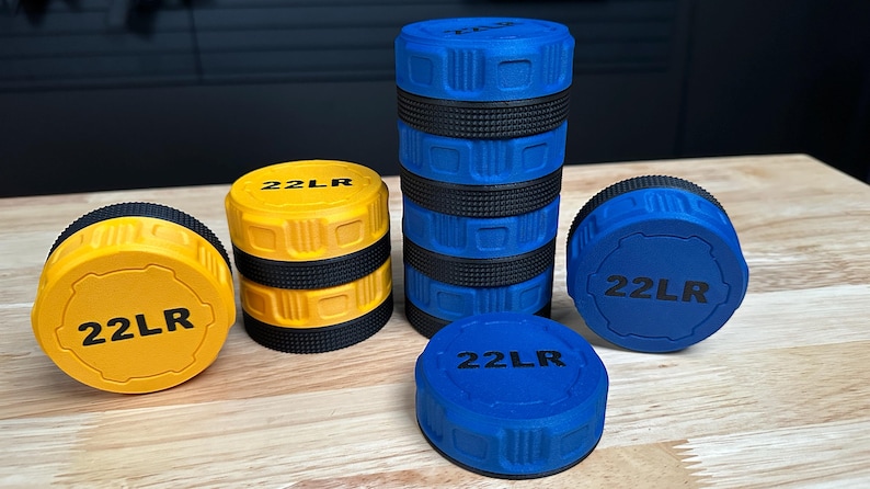 May include: A collection of cylindrical storage containers for 22LR ammunition, featuring yellow and blue plastic bodies with black textured grip bands. Each lid is embossed with the text 22LR in black, showing various stacking configurations.