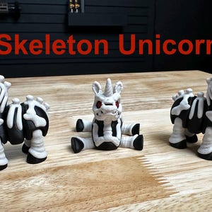 Puede incluir: Tres peque&ntilde;as figuras de unicornio con cuerpos negros y patrones esquel&eacute;ticos blancos. Cada figura tiene un cuerno, ojos rojos y una pose distinta. El texto "Skeleton Unicorn" aparece en color rojo sobre las tres figuras.