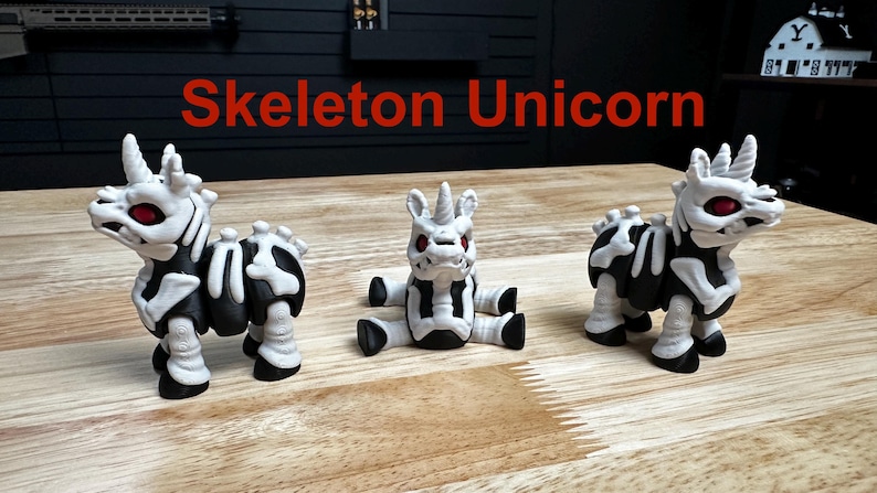 Puede incluir: Tres peque&ntilde;as figuras de unicornio con cuerpos negros y patrones esquel&eacute;ticos blancos. Cada figura tiene un cuerno, ojos rojos y una pose distinta. El texto "Skeleton Unicorn" aparece en color rojo sobre las tres figuras.