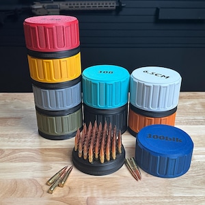 May include: A collection of colorful cylindrical containers with ribbed lids, stacked and arranged on a wooden surface. The containers are in various colors, including red, yellow, gray, teal, white, orange, and blue. Some containers have text on the lids. A display of bullets is in the center.