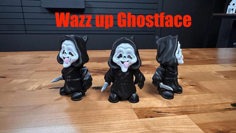 Puede incluir: Tres figuras de Ghostface con m&aacute;scaras blancas, t&uacute;nicas negras con capucha y cuchillos plateados, cada una con la lengua fuera. El texto Wazz up Ghostface aparece en letras rojas sobre las figuras.
