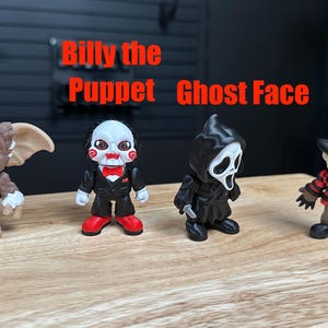 Puede incluir: Cuatro peque&ntilde;as figuras de vinilo dispuestas en fila. De izquierda a derecha: Gismo, una criatura marr&oacute;n y blanca; Billy the Puppet, con traje negro y pajarita roja; Ghost Face, con t&uacute;nica negra con capucha; y Freddy, con su&eacute;ter a rayas y sombrero.