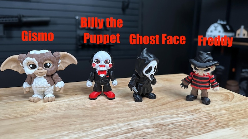 Puede incluir: Cuatro peque&ntilde;as figuras de vinilo dispuestas en fila. De izquierda a derecha: Gismo, una criatura marr&oacute;n y blanca; Billy the Puppet, con traje negro y pajarita roja; Ghost Face, con t&uacute;nica negra con capucha; y Freddy, con su&eacute;ter a rayas y sombrero.